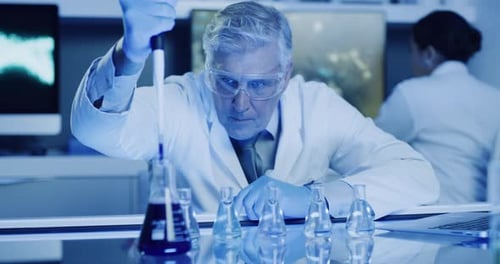 Mature laboratory scientist testing phenolphthalein chemical reaction with a beaker