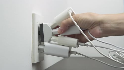Hand inserting electrical plugs into outlet. Electrical overload