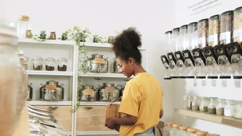 A young woman is shopping in refill store with reusable bag, zero-waste grocery.