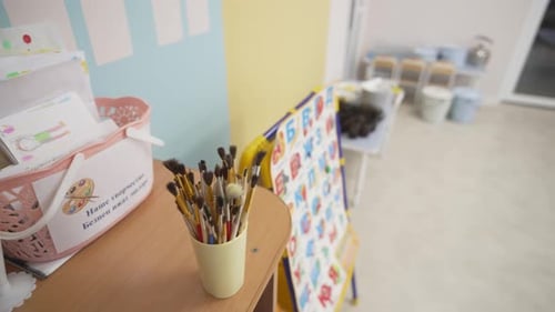 Paintbrushes Stand in Plastic Cup on Desk in Classroom