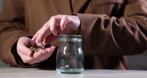 Woman Saving Money and Putting Coins into Jar