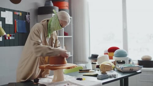 Stylish Woman Works on Hat in Bright Workshop