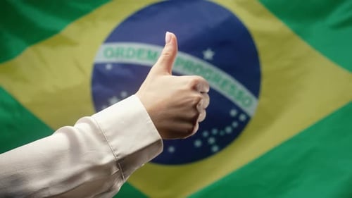 Frau macht Handzeichen wie eine Daumen-Hoch-Geste auf brasilianischem Flaggenhintergrund Brasilien Korrekt Perfekt