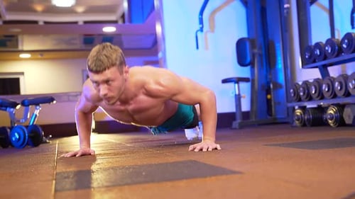 young male shirtless bodybuilder doing push-ups from the floor in a sports club or gym.
