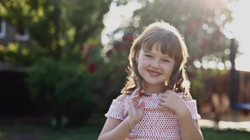 Front View of Adorable Little Girl with Hairstyle is Smiling with Her Outdoors on Summer Day