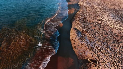 Numerous footsteps cover the sandy beach. Waves splash on the shore at sunset.