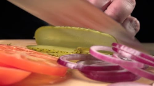 Man prepares fresh vegetables for unhealthy hamburger on wooden desk slow motion