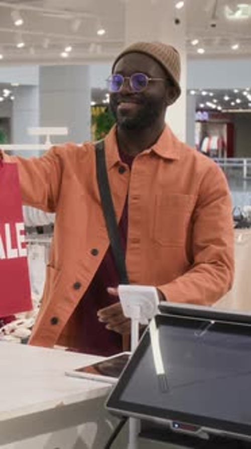 Vertical of Customer Taking Two Red Shopping Bags from Cashier in Store