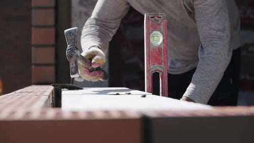 builder lays brick wall, hands close-up, hammer in hand