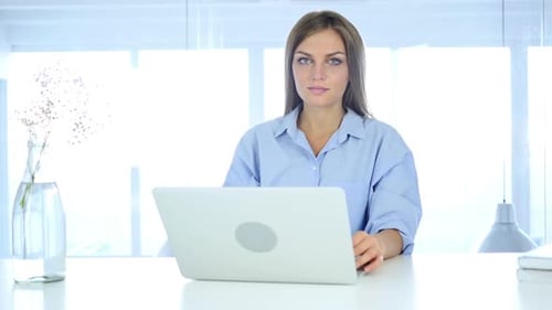 Smiling Woman Gives OK Gesture at Office Desk