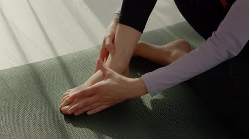 Woman Massaging Foot and Ankle on Yoga Mat