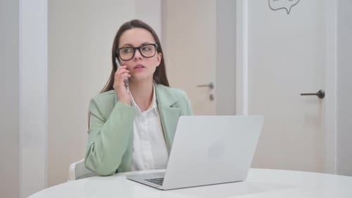 Young Woman Working at Computer and Talking on Phone