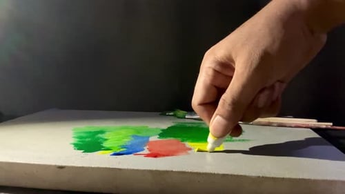 Hand Squeezing Yellow Paint onto Canvas with Colors