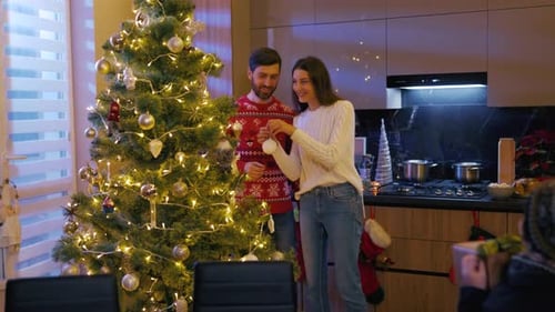 Couple decorates Christmas tree while family gathers