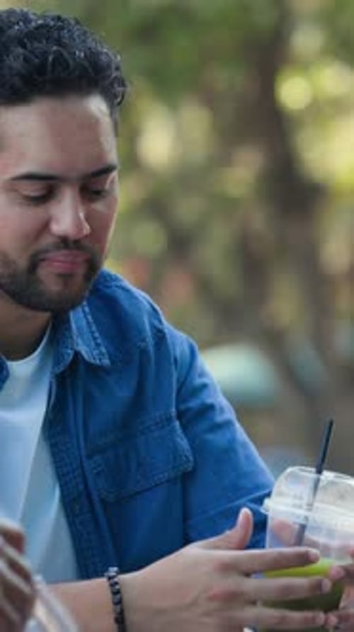 Homme sirotant une boisson verte brillante, plissant au goût, faisant tourner la tasse et faisant des gestes pendant la conversation
