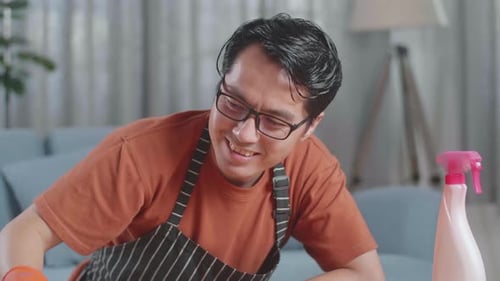 Close Up Of Asian Male Housekeeper With An Apron Cleaning The Table By The Spray At Home