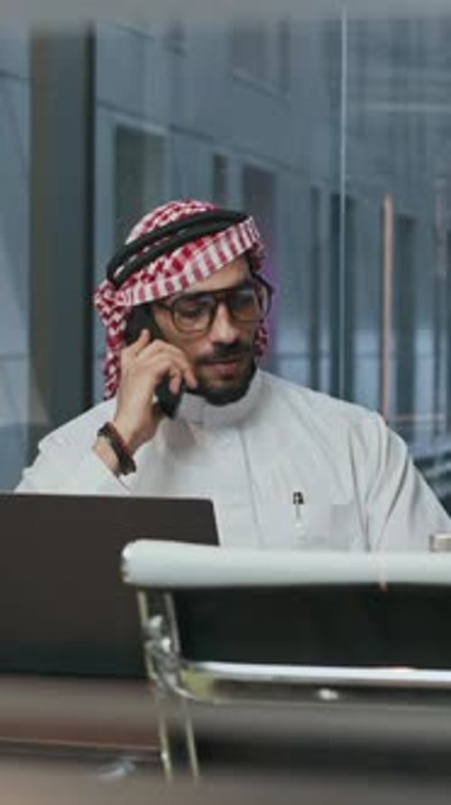 Middle Eastern Entrepreneur Calling on Smartphone by Laptop at Office