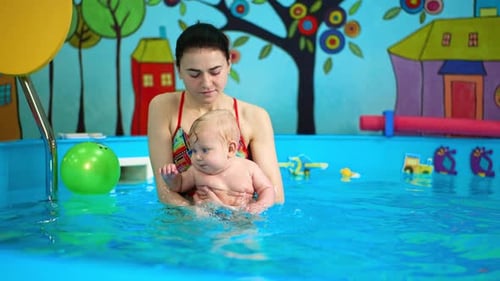 Caucasian brunette woman holds a baby in the swimming pool.