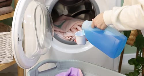Woman pouring detergent into washing machine with laundry indoors, closeup