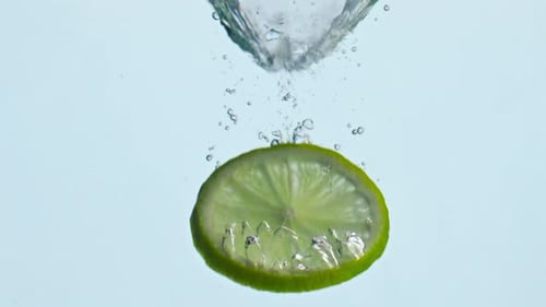 Lime slice falling into clear water bubbles