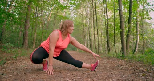 Caucasian women in sportswear stretching legs and exercising in the forest trail.