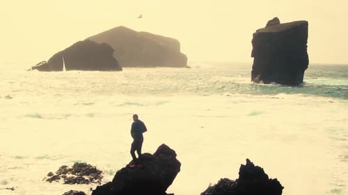 Man silhouette standing on rock with open arms against monsteiros beach in Sao Miguel, Azores Island