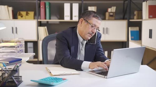 Man Talking on Phone and Working on Laptop