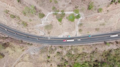 Aerial drone view: a curved highway cutting through arid terrain. Cars and trucks traverse the road