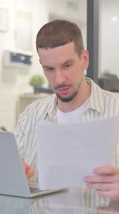 Man Working at Home at Laptop with Documents