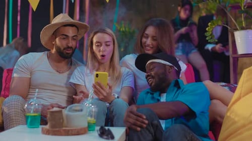 Friends Reacting to Phone at Outdoor Party at Night