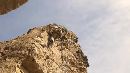 A Man is Climbing a Rock Wall with a Rope