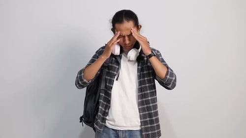 Young Asian college student having headache and massaging temples isolated on white studio