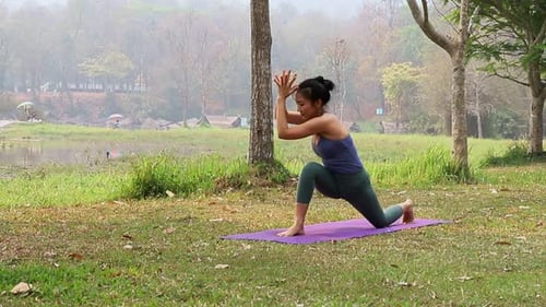 Asian woman practicing yoga in Revolved Side Angle Pose in outdoor park. Stabilizes the outer hip.