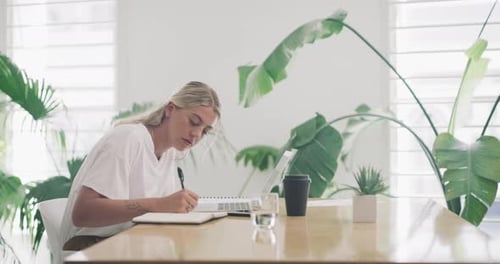 4k video footage of a young businesswoman writing notes and working on a laptop in an office