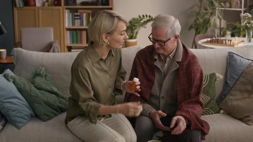 Woman Gives Elderly Man Medicine on Couch
