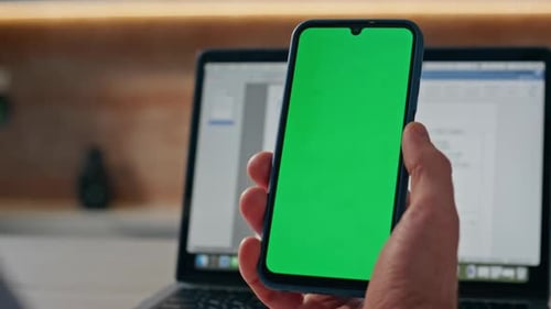 Hand Holding Mobile Phone with Green Screen, Laptop
