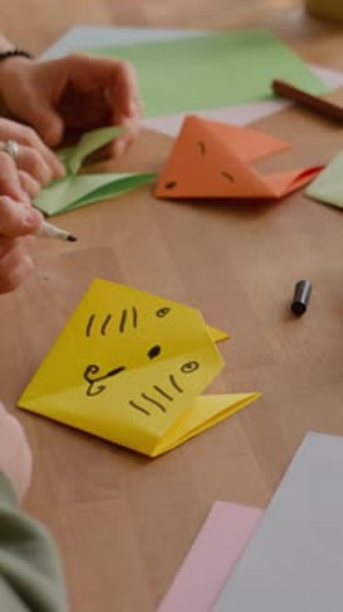 Child Draws on Paper Origami Craft at Table
