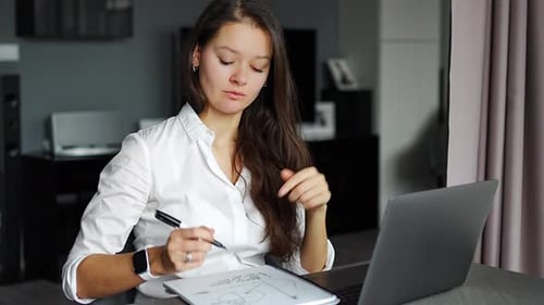 Woman Working on Laptop and Writing in Notebook