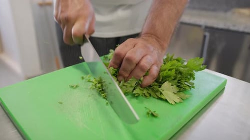 Cook Is Chopping Parsley With Knife On A Green Chopping Board