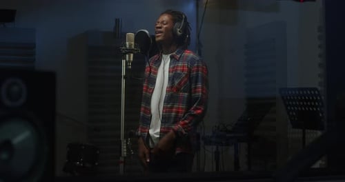 Portrait of a Professional Male Black Singer with Headphone Recording a Song in a Studio.