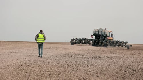 Farmer Walking Towards Tractor A Farmer Wearing a Highvisibility Vest Walks Across a Freshly Plowed