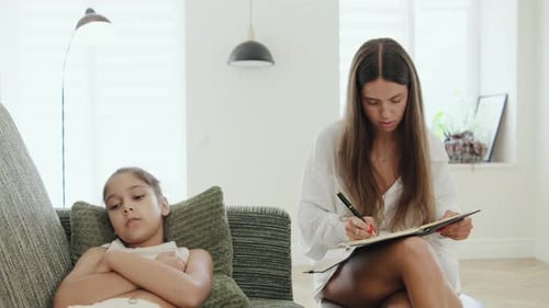 Therapist is Sitting with a Notebook Writing During a Session While a Young Girl Sits Nearby with