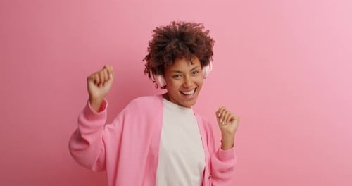 Excited Woman Dancing with Headphones on Pink Background