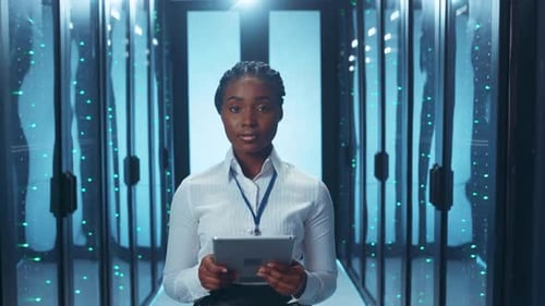 A Woman Standing in a Data Center is Holding a Tablet and Engaging with Technology