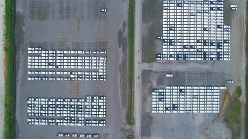 Drones flying above factory parking lot, new cars unsold