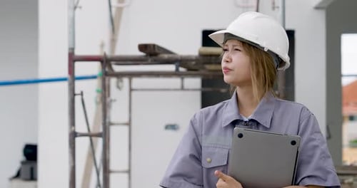 Asian female engineer walks slowly with clipboard near scaffold, performing construction site