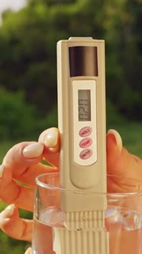 Vue rapprochée du verre à main féminin avec testeur numérique de qualité de l'eau montrant vingt ppm ppm