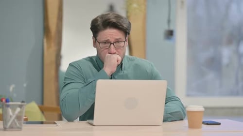 Man Coughing While Working on Laptop at Desk