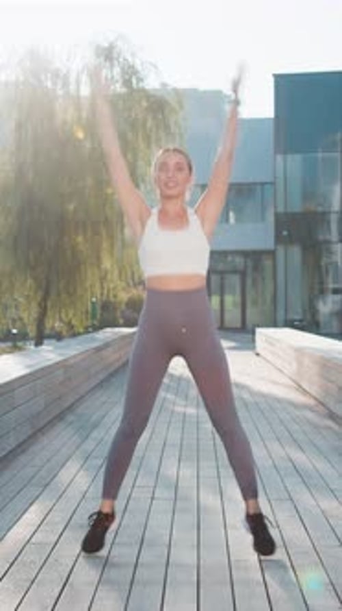 Caucasian Sporty Young Woman Jumping on Bridge Warmup Before Jogging in City Park on Sunny Day