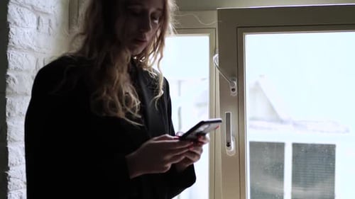 Woman Standing by Window Using Mobile Phone